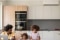L'image montre un jeune père et ses deux filles dans une cuisine, avec l'unité intérieure d'un système de climatisation Carrier sur le mur.