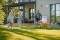 Une famille profitant de son jardin devant une maison moderne équipée d'une pompe à chaleur air-eau Carrier fixée au mur.