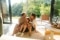 L'image montre une famille avec deux enfants assis par terre dans le salon devant une porte-fenêtre ouverte, se serrant joyeusement dans les bras les uns des autres.